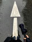 Person standing on rain-wet pavement facing a painted arrow pointing forward, symbolizing career change, uncertainty, and moving into a new chapter as a real estate agent.