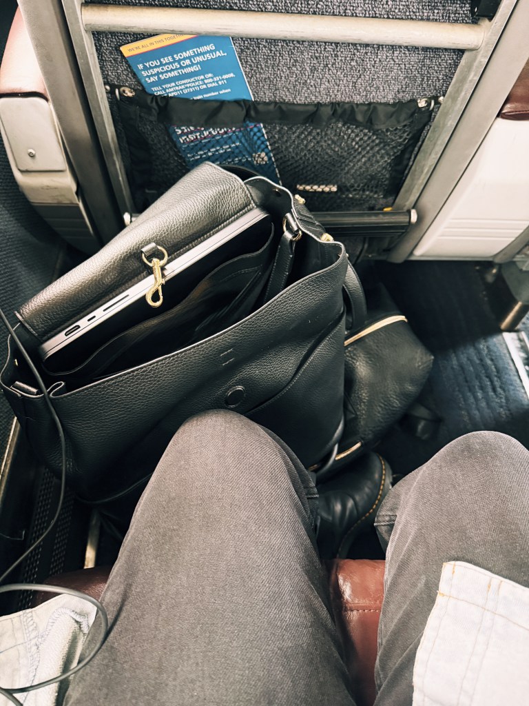 A black leather bag balanced on lap in a cramped Amtrak business class seat