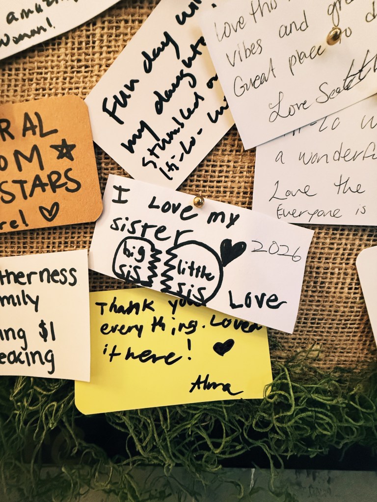 A handwritten note pinned to a burlap board that reads "I love my sister" with a doodle of a heart split into two halves labeled "big sis" and "little sis"
