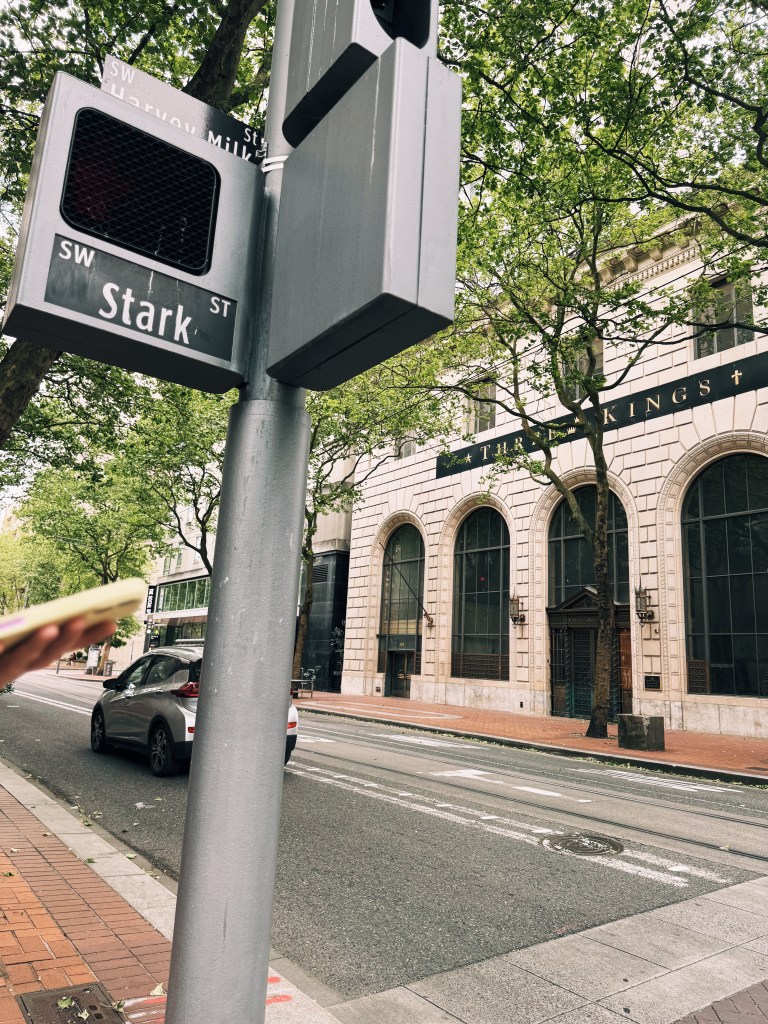 A Stark Street sign on a tree-lined Portland street, with a historic arched building across the way
