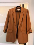 An empty camel-colored blazer hanging on a black hanger, backlit by warm interior light