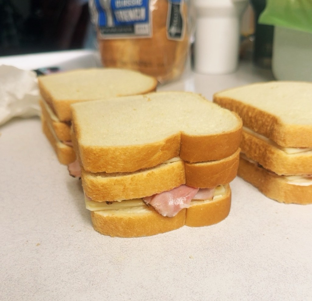 Three homemade Monte Carlo sandwiches stacked with ham and cheese on thick white bread before cooking